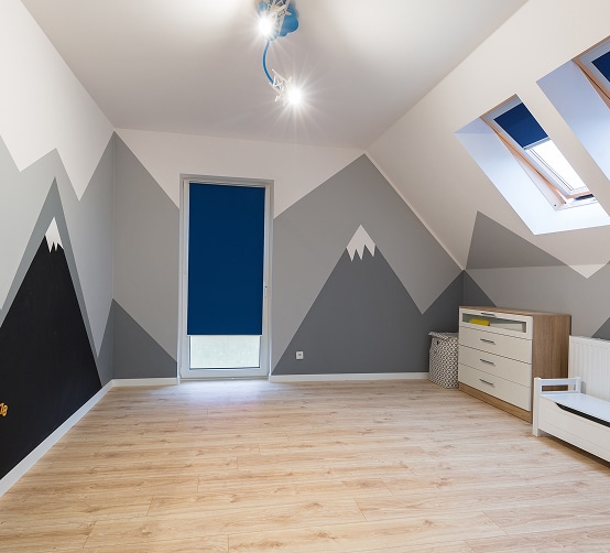 Chambre mansardée pour enfant décorée de montagnes stylisées en noir, gris et blanc, avec un sol en bois clair et un volet bleu foncé.