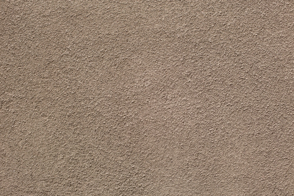 Gros plan détaillé sur la texture rugueuse et uniforme d'un mur en crépi beige taupe. Surface granuleuse idéale pour façade extérieure.