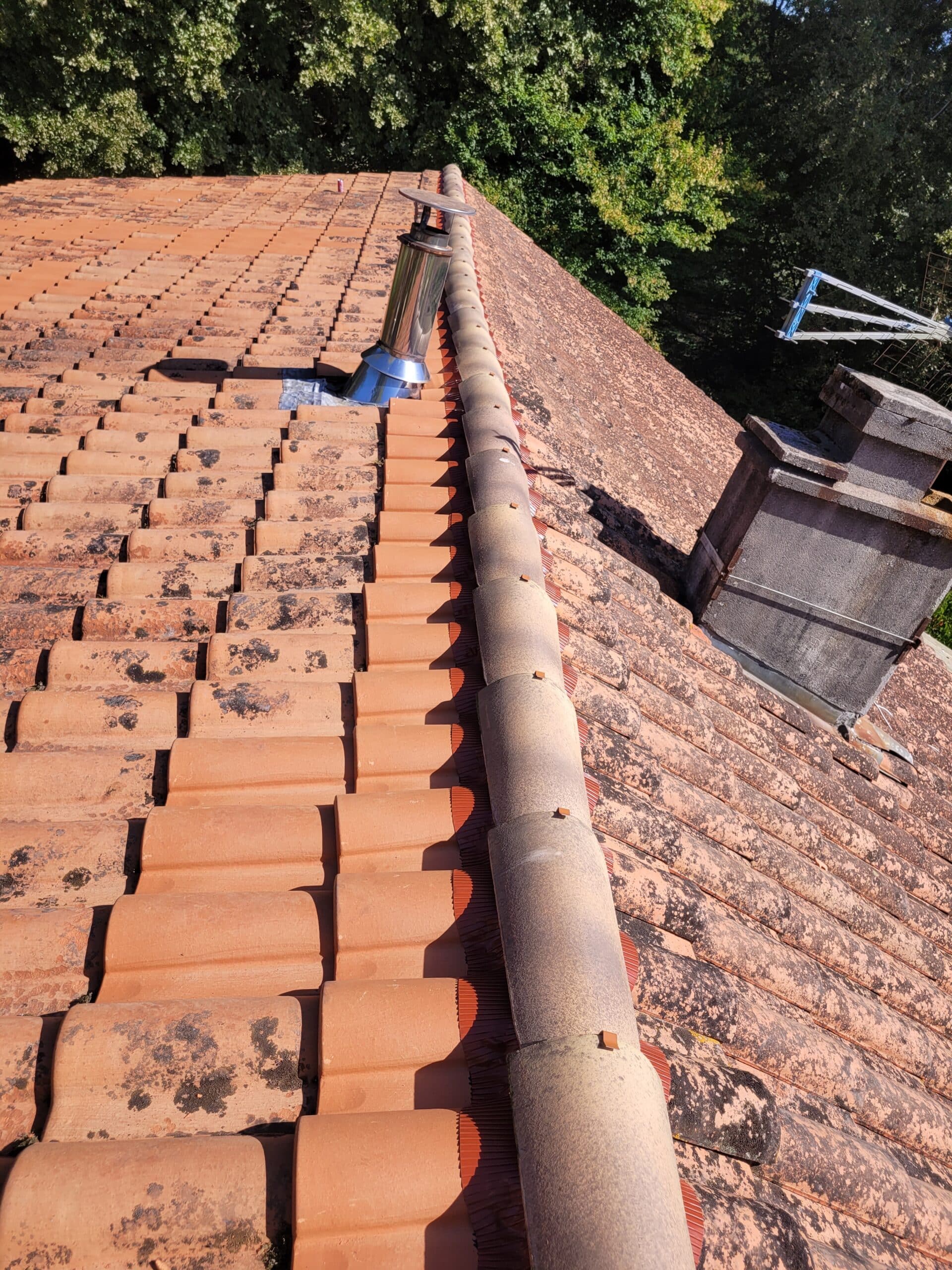Toit en Tuiles Anciennes : Faîtage, Cheminée et Lichen. Toit en tuiles de terre cuite anciennes et propres, faîtage avec aération et nouvelle cheminée en inox. Forte présence de lichen sur la pente droite.